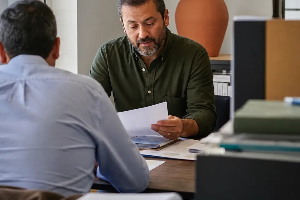 Finance lead reading a printed budget pack at a meeting table