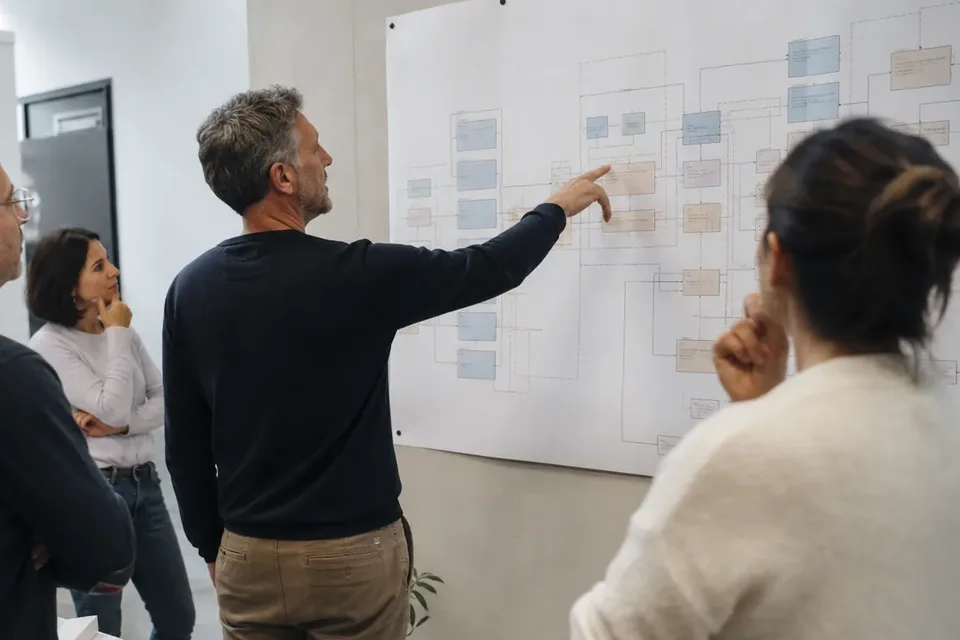 Finance lead pointing at a planning chart on the wall while three colleagues listen