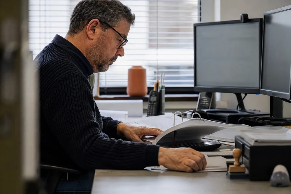 Realistic photo of an adult accountant reconciling ledger entries on a dual monitor setup in a quiet office