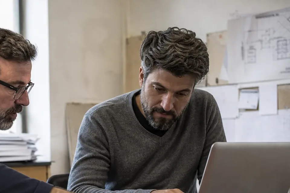 Senior engineer working on a laptop at a desk with system diagrams pinned behind